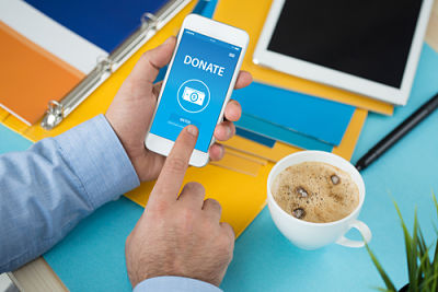 Picture of male making a donation on his cell phone, while sitting at a desk.